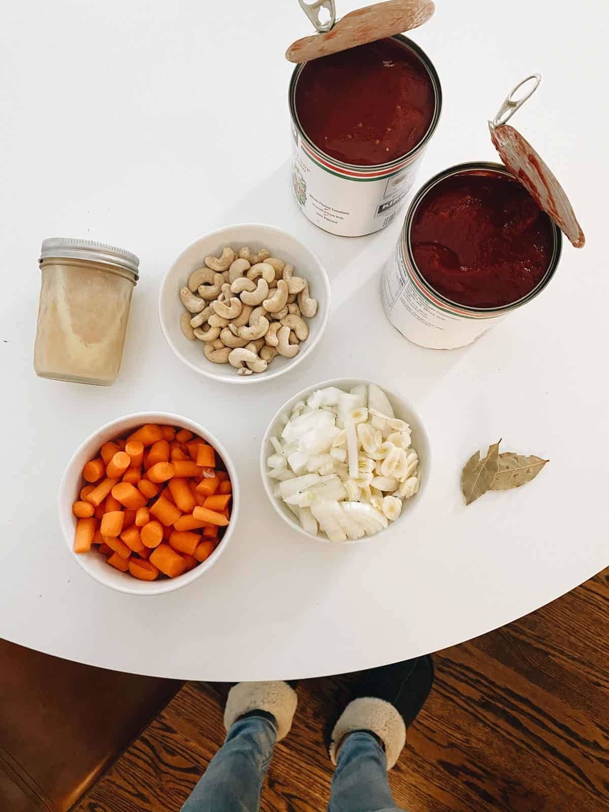 Canned tomatoes, cashew, carrots, garlic, bay leaves on a table to make tomato soup.