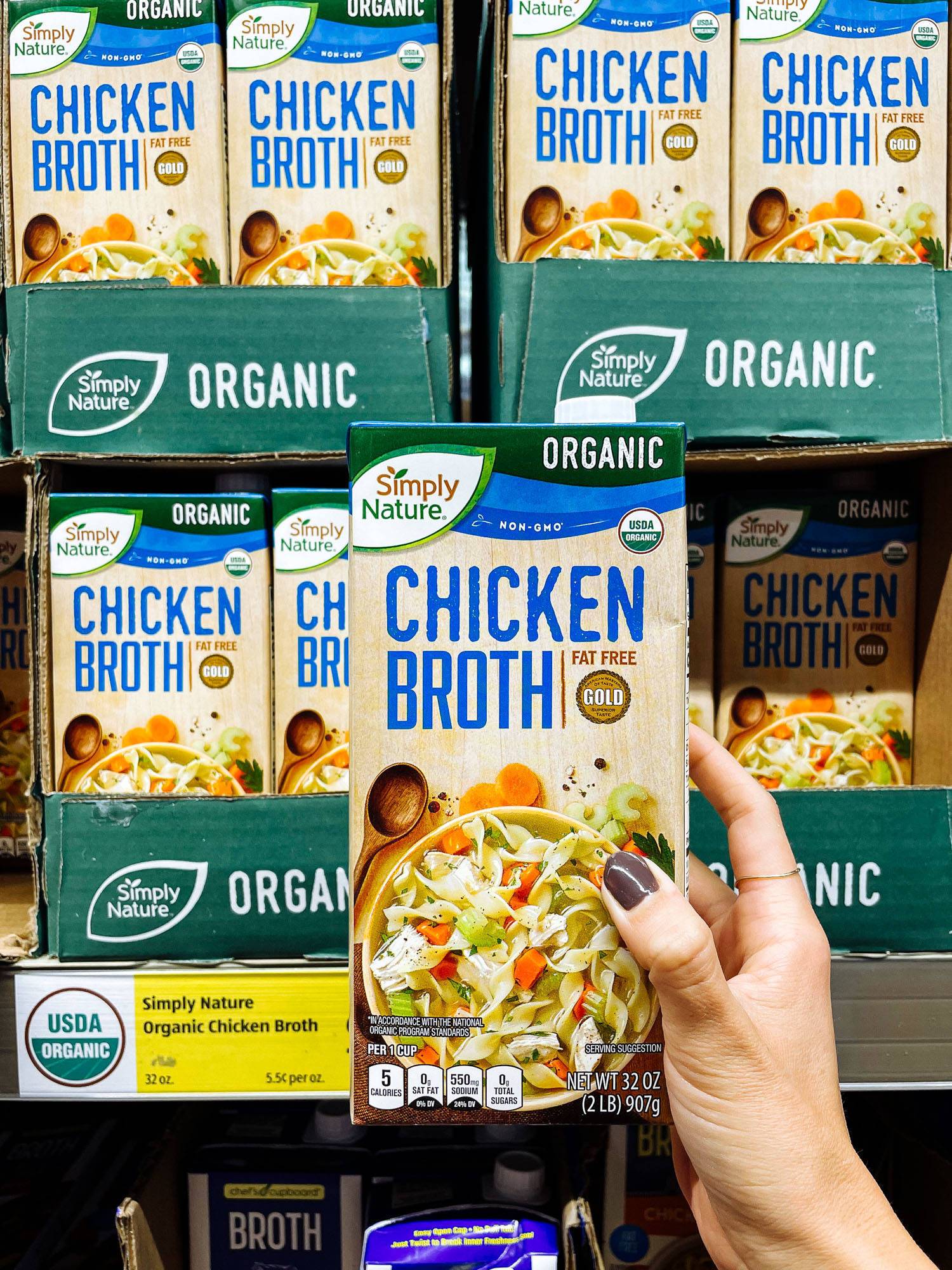 White hand holding chicken broth carton from ALDI.