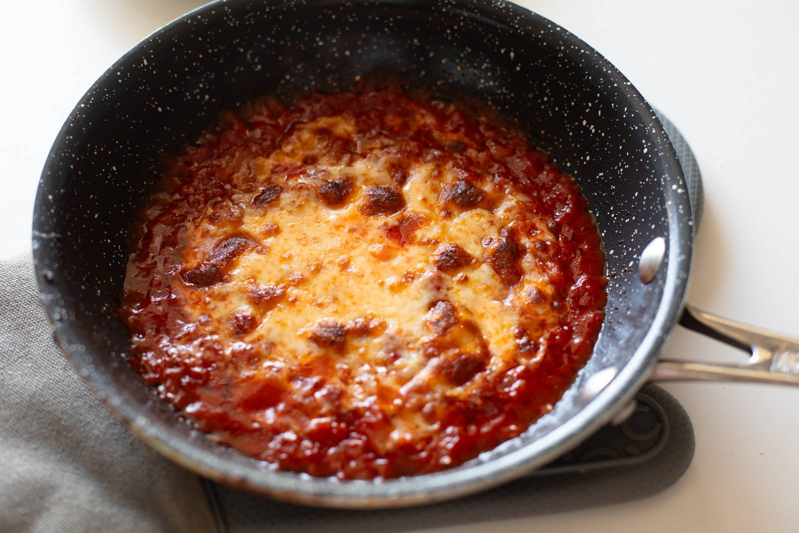 Bubbly cheese on top of sauce in a pan.