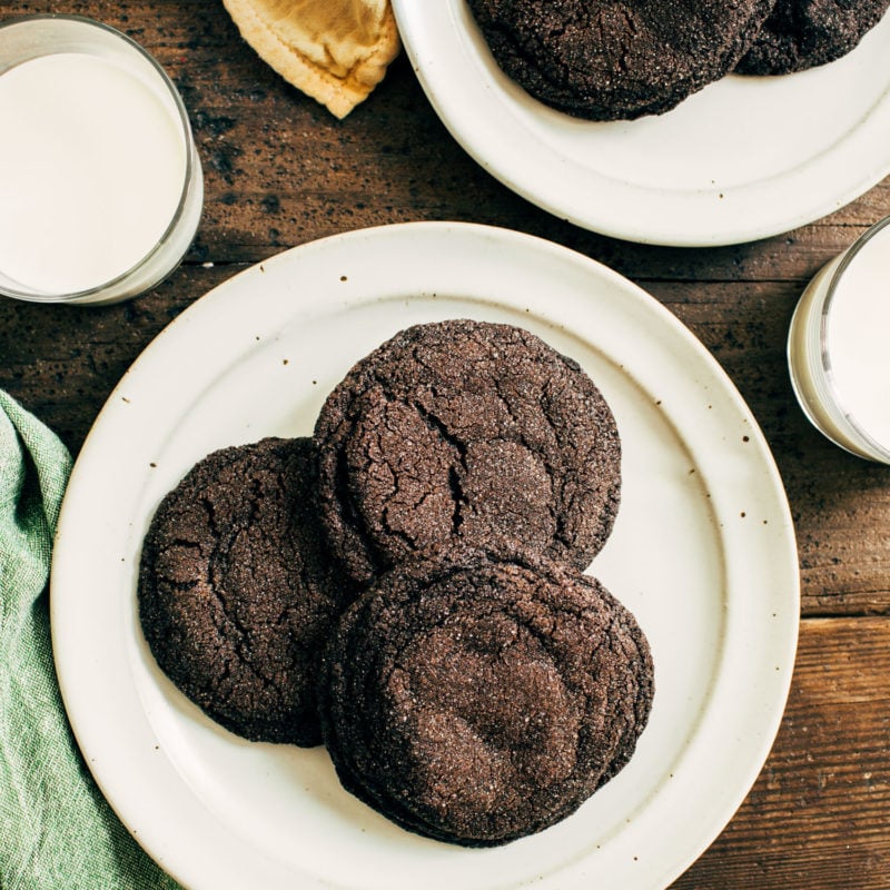 Dark chocolate cookies on a plate next to a glass of milk.