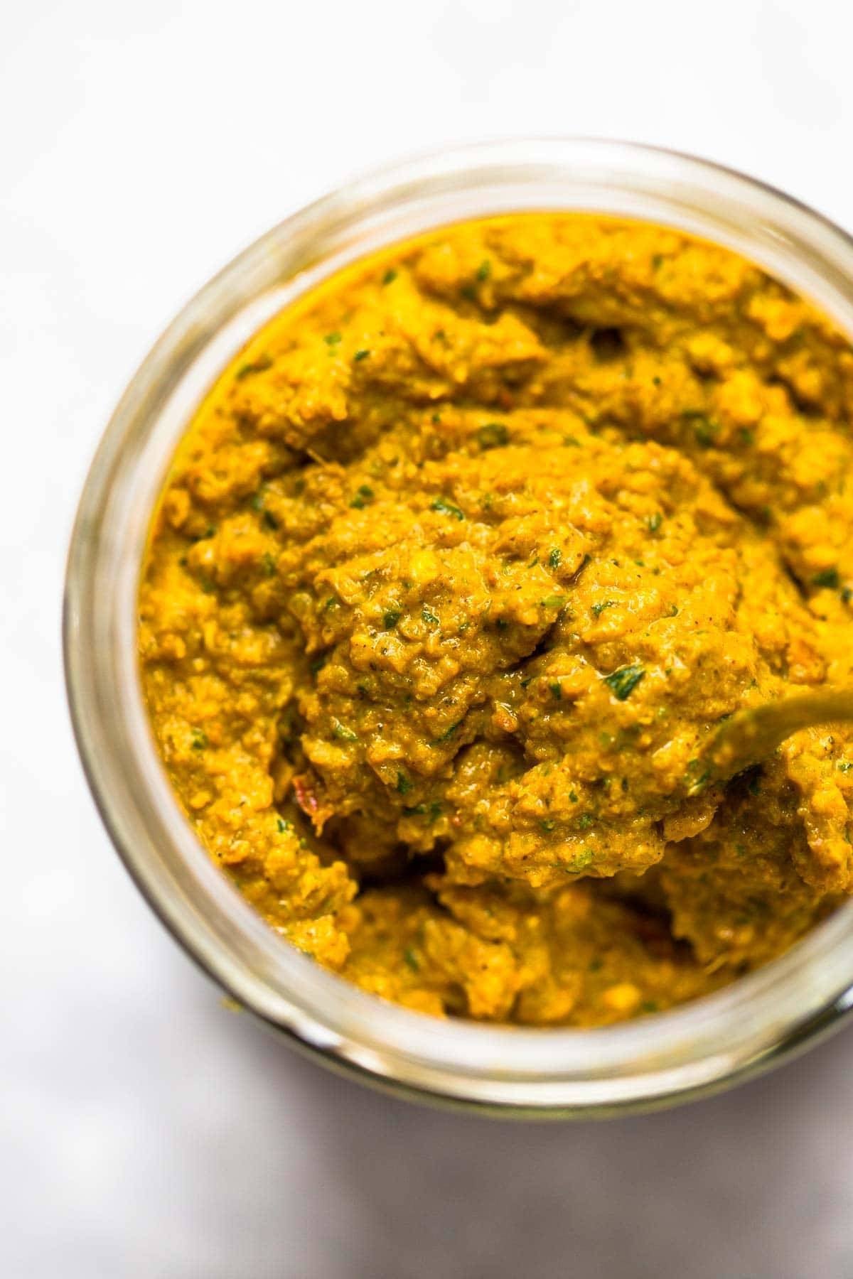 Homemade yellow curry paste in a jar with a spoon.