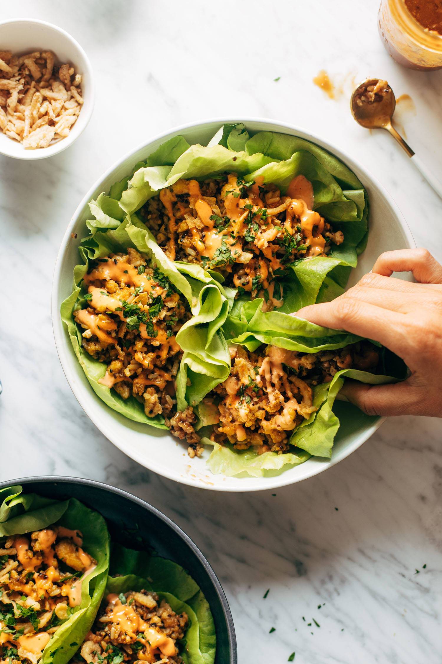 White hand grabbing a tofu and brown rice lettuce wrap with peanut sauce drizzled on top.